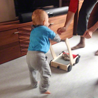 Baby läuft mithilfe eines Lauflernwagens von PlanToys in die Arme seiner Mutter.