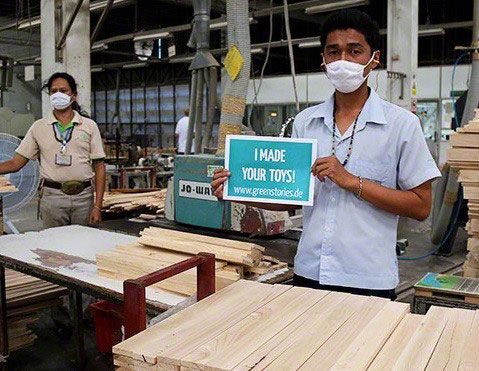 Arbeiter in der Fabrik von PlanToys in Thailand hält ein Schild hoch mit der Aufschrift "I made your toys°!.