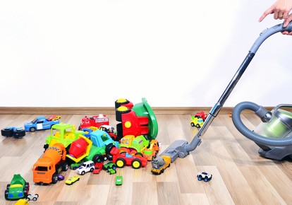 Es liegen so viele Spielzeugautos in verschiedenen Formen, Farben und Größen auf dem Boden, dass die Mutter mit dem Staubsauger nicht durchkommt.