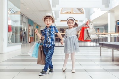 Junge und Mädchen stehen schick gekleidet und mit vielen Einkaufstüten in einem Shopping-Center.