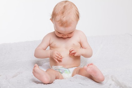 Baby sitzt mit einer Windel auf einer Decke und schaut sich seine Haut an