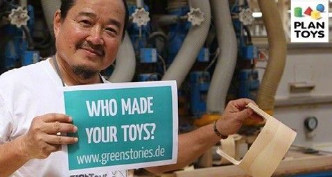 PlanToys-Gründer Vitool hält einen Rohling des Lauflernwagens und ein Schild mit der Aufschrift "Who made your toys?"