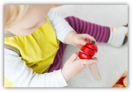 Kind hält eine schneidbare Holz-Tomate in der Hand
