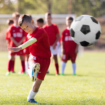 Ein Junge schießt einen Fußball, die anderen aus seiner Mannschaft stehen hinter ihm.