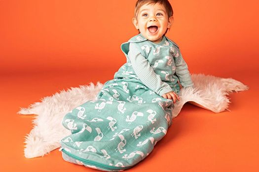 lachendes Kleinkind in einem türkisen Schlafsack mit Tukan-Vögeln drauf