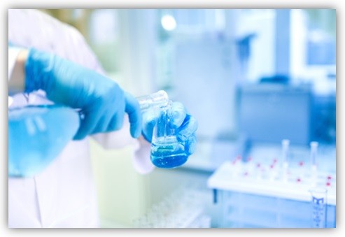Person füllt in einem Labor eine Flüssigkeit in ein Glas-Gefäß