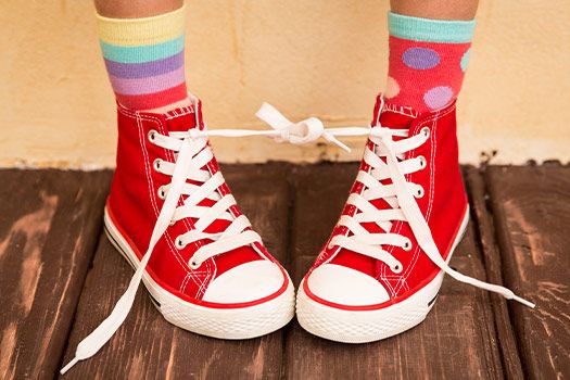 Kinderfüße in bunten Socken und roten Chucks, deren Schnursenkel vom rechten und linken Schuh zusammengebunden sind.