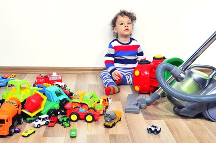 Junge sitzt auf dem Boden und starrt in die Luft. Viele verschiedene Spielzeugautos liegen auf dem Boden.