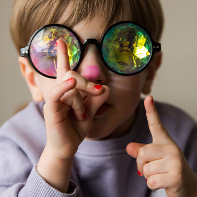 Junge mit bunter Nase, rot lackierten Fingernägeln und einer Kaleidoskop-Brille auf