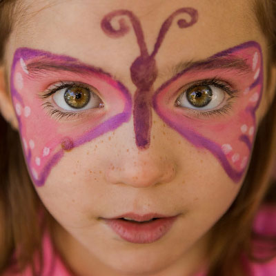 Nahaufnahme des Gesichts eines Mädchens, das mit der Kinderschminke einen Schmetterling aufgemalt bekommen hat, dessen Flügel über die Augen gehen.