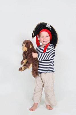 Junge mit heller Hose, blauweiß-getreiftem Langarm-Shirt und einem Piratenhut gekleidet. Auf dem Arm trägt er einen großen Kuschel-Affen.