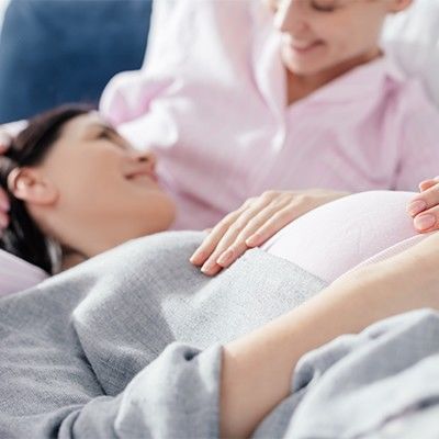 Zwei Frauen schauen sich glücklich an, während sie die Hände auf dem auch der einen haben, die schwanger ist.