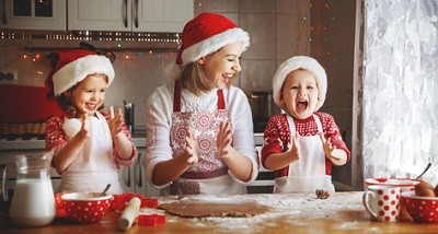 Mutter hat mit ihren zwei Kindern Spaß beim Plätzchenbacken. Alle drei tragen Weihnachtsmützen.