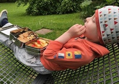 Junge sitzt draußen auf einem Liegestuhl und isst Snacks aus einer Edelstahl Brotdose