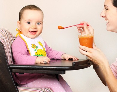 Mutter füttert ihr Baby, das in einem Stuhl sitzt, mit Brei