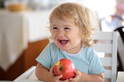 Lachendes Kleinkind, dass einen angebissenen Apfel in den Händen hält
