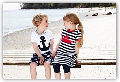 Mädchen und Junge sitzen auf einer Bank an einem Strand und tragen maritime Styles von Fred´s World