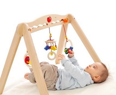 Baby liegt unter einem Spielbogen und Greift nach den hängenden Elementen.