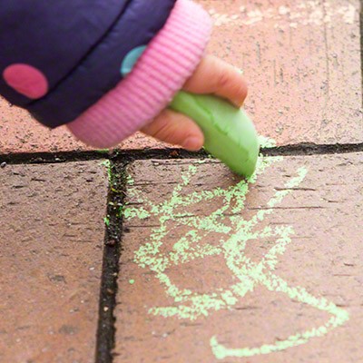 Kinderhand malt mit grüner Kreide auf einem gepflasterten Weg