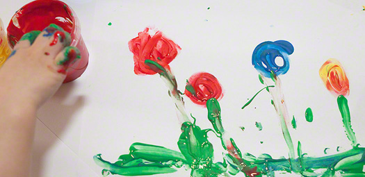 Kind malt mit Fingerfarben eine Blumenwiese