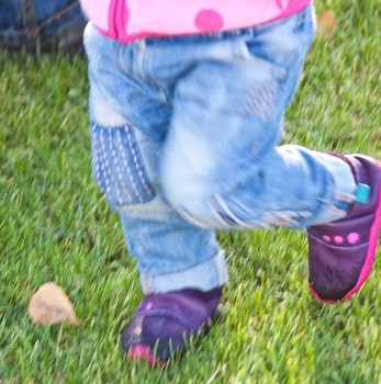 Kind läuft mit den Lauflernschuhen über den Rasen