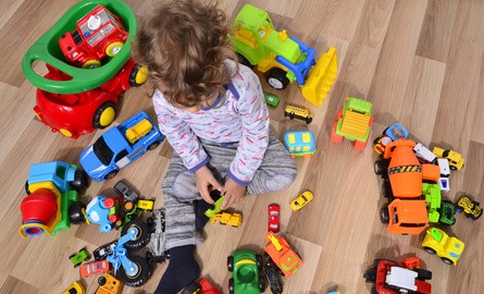 Kind sitzt zwischen vielen Spielzeugautos auf dem Boden