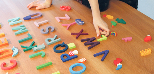 Kind spielt auf dem Boden und ordnet die Lernfiguren den Holzbuchstaben zu