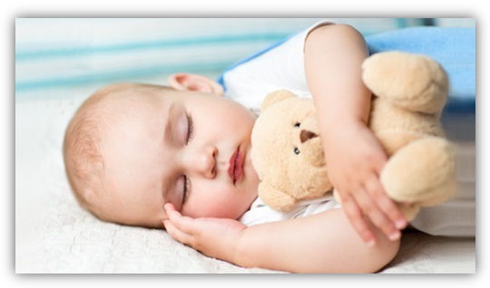 Baby schläft mit Kuscheltier-Bär im Arm