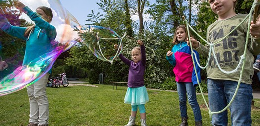 Kinder unterschiedlichen Alters, wie sie versuchen, Riesenseifenblasen herzustellen