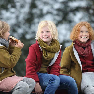 Drei Kinder sitzen draußen und tragen Wollkleidung von Disana.