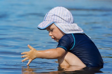 Kind hockt in UV-Schutzkleidung im seichten Wasser