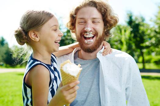 Vater und Tochter lachend beim Eisessen. Der Vater hat Eis an der Nase und um den Mund.