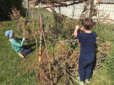 Zwei Kinder bauen im Garten ein Haus aus Stöcken