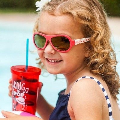 Mädchen am Pool mit Becher in der Hand und Sonnenbrille auf der Nase