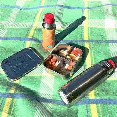 Zwei isolierte Flaschen liegen neben einer Dose auf einer Picknick-Decke in der Sonne.
