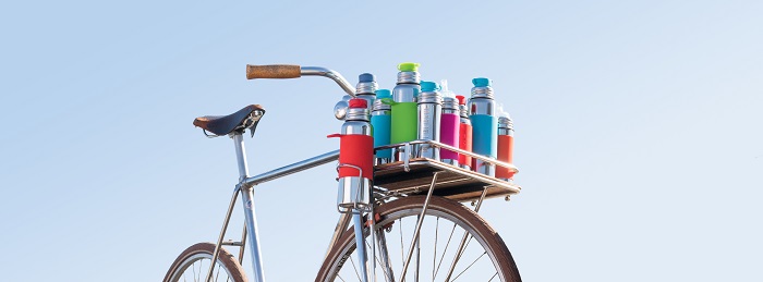 Fahrrad mit Ablagefläche vorne, die voll ist mit bunten Pura kiki Trinkflaschen