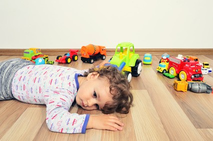 Kind liegt fertig auf dem Boden, um es herum ist Spielzeug verteilt