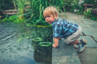 Kleines Kind hockt gefährlich nah am Rand eines Gartenteichs.
