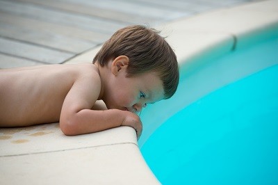 Kleiner Junge liegt am Beckenrand eines Pools und schaut über die Kante ins Wasser