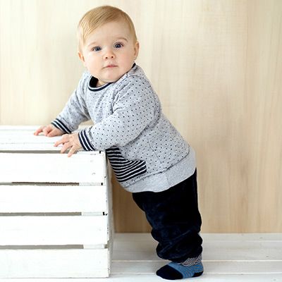 Ein Baby hält sich im Stehen an einer Kiste fest.