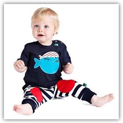 Kind sitzt auf dem Boden und trägt ein T-Shirt mit einem Piraten-Fisch und eine blau-weiß-gestreifte Hose mit roten Aufnähern an den Knien