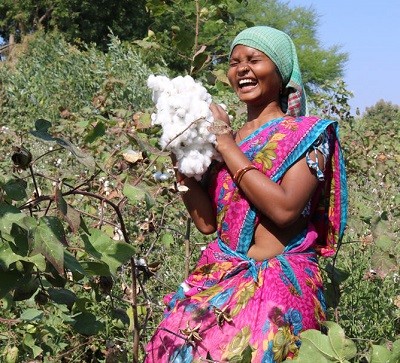 Frau steht lachend mit geernteter Bio-Baumwolle auf dem Feld
