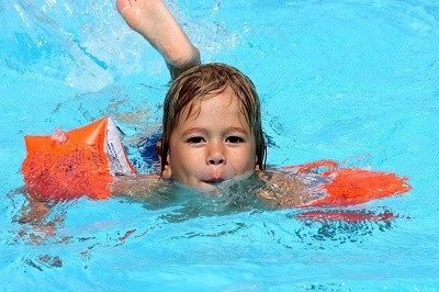 Kind mit Schwimmflügeln im Wasser eines Schwimmbeckens