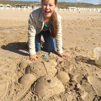 Strahlendes Mädchen, die ihrem Marienkäfer aus Sand präsentiert