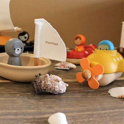 Verschiedenes Badespielzeug von PlanToys liegt mit Muscheln auf einem Tisch