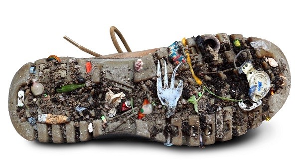 Ein Schuh, unter dessen Sohle sich so einiges angesammelt hat: eine Plastik-Gabel, Zigarettenstummel usw.