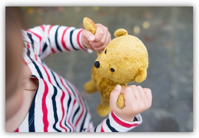 Kind mit Teddybär in den Händen, es zieht an den Armen des Bären